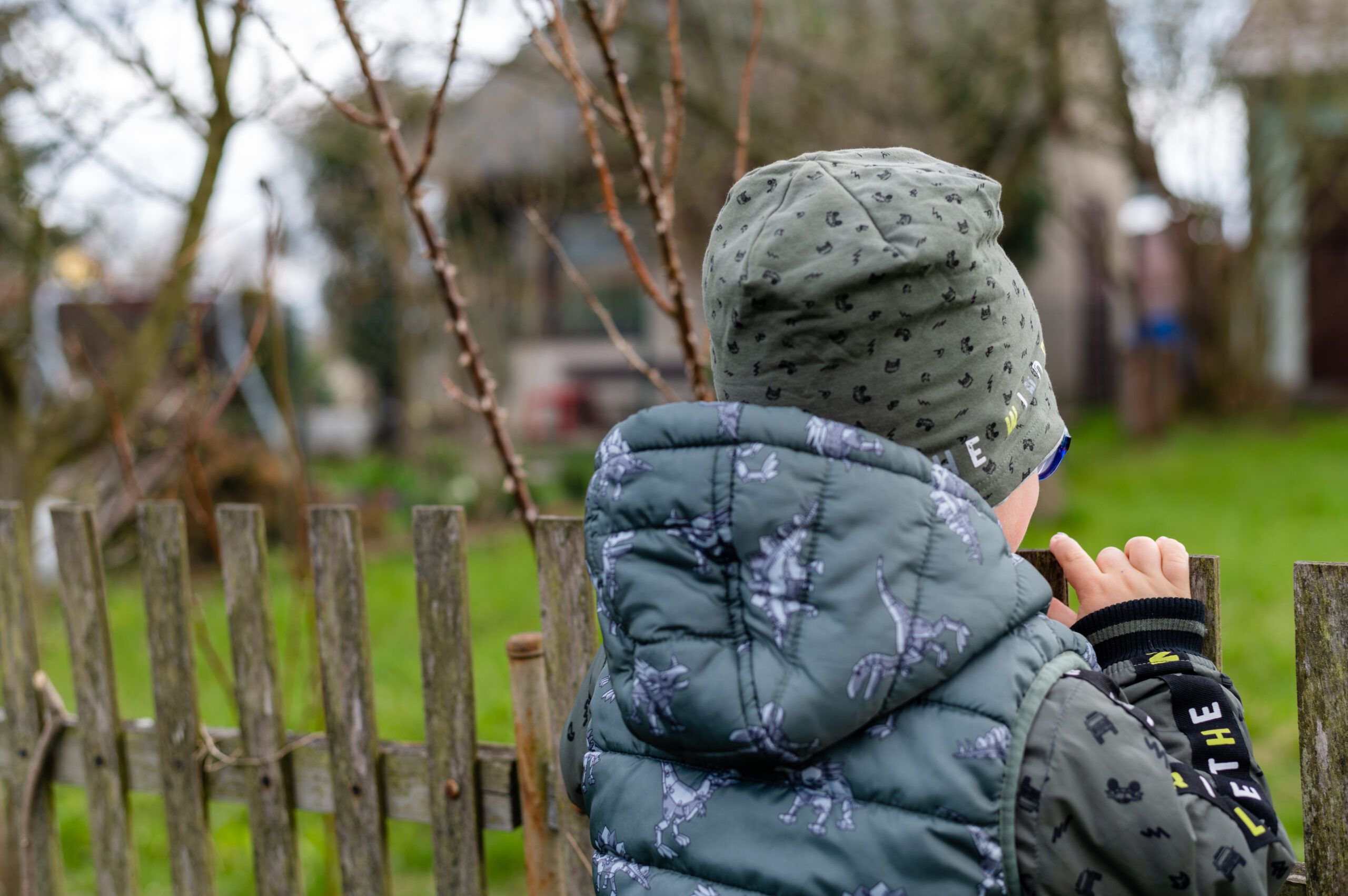 Boy in a grey hood and grey hooded coat with his back to the camera looking away