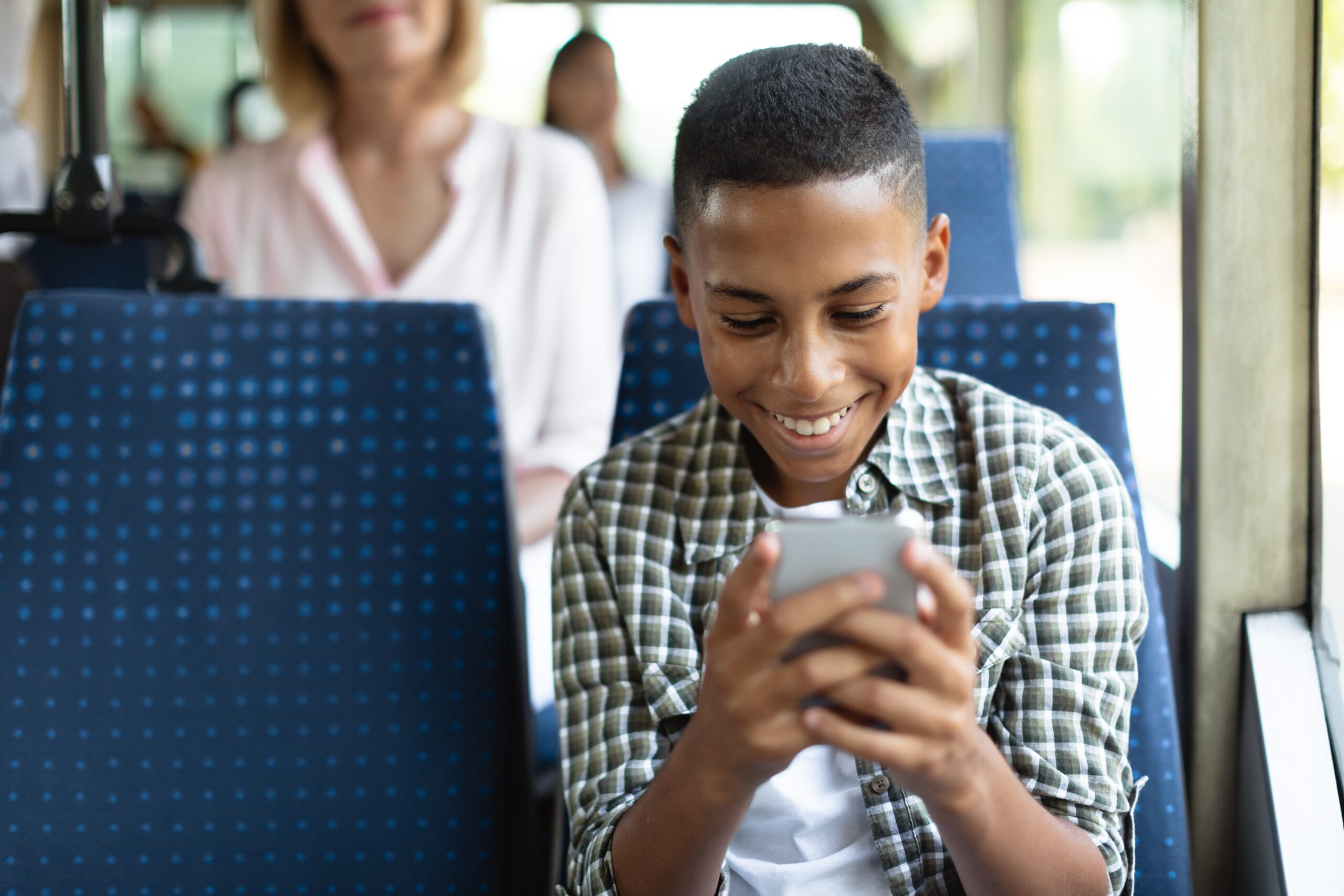 Boy sat on a bus looking at his phone smiling