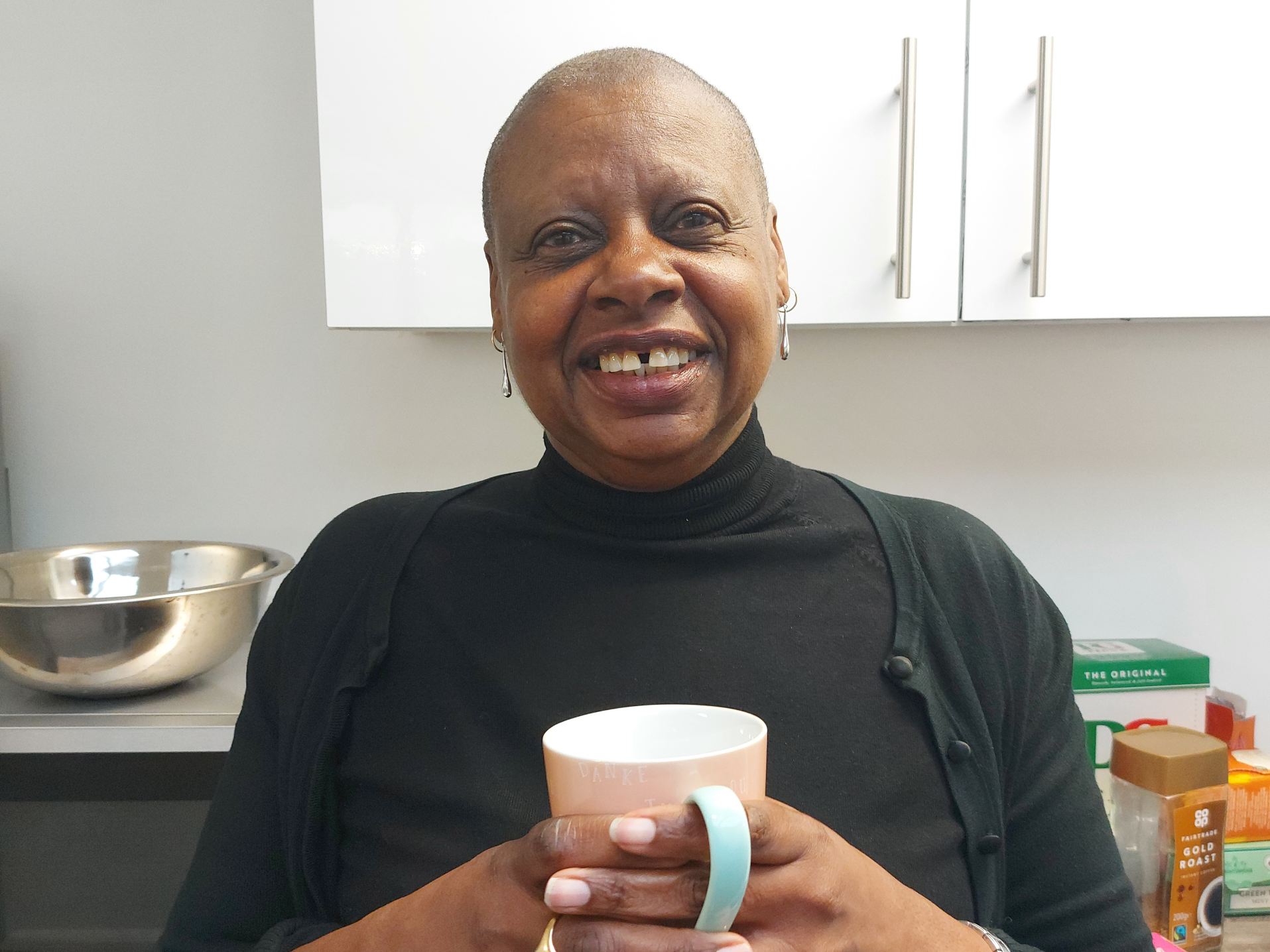 Dorrett holding a cup of tea in front of the kitchen and smiling at the camera