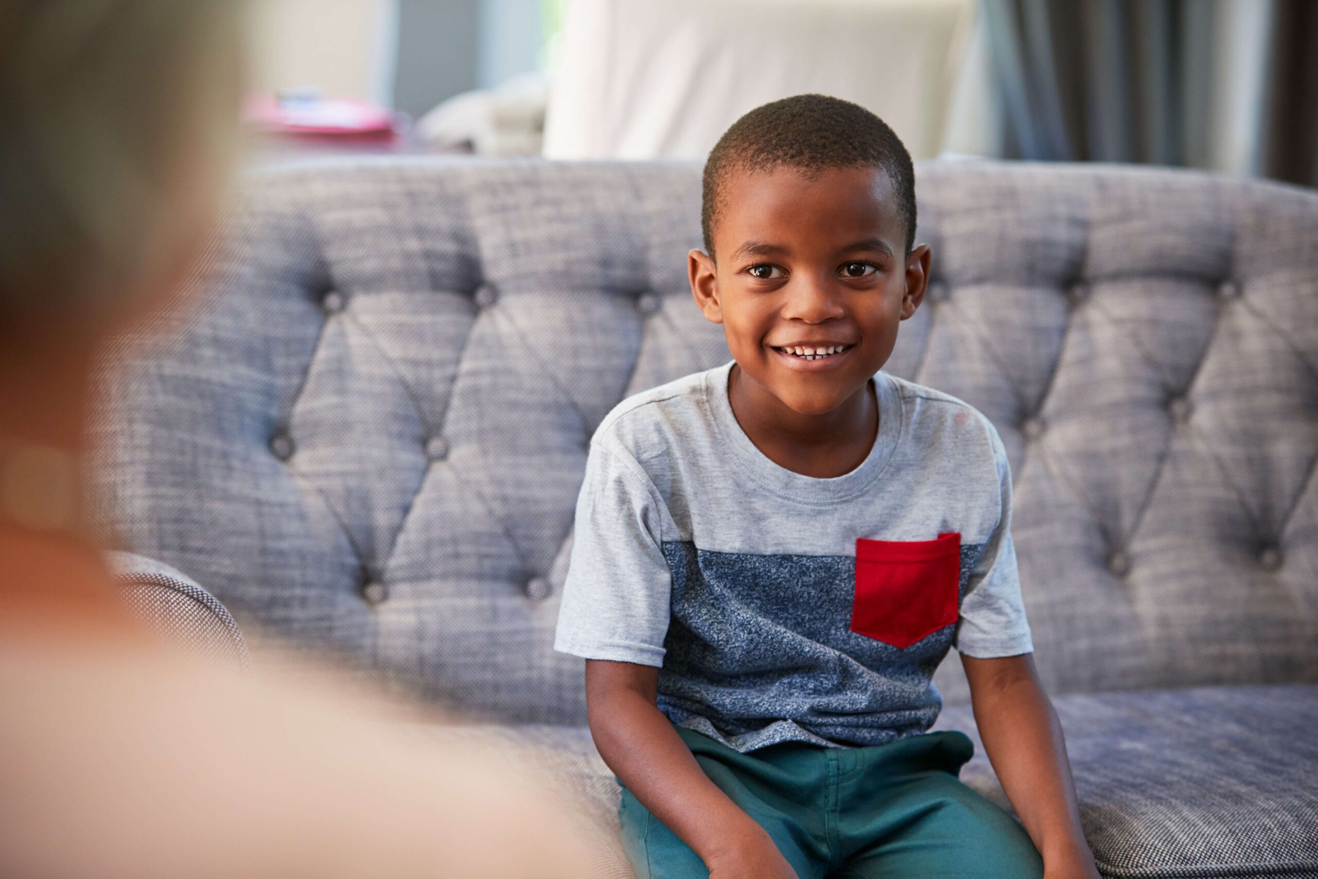 Boy sat on a sofa smiling at an adult out of shot